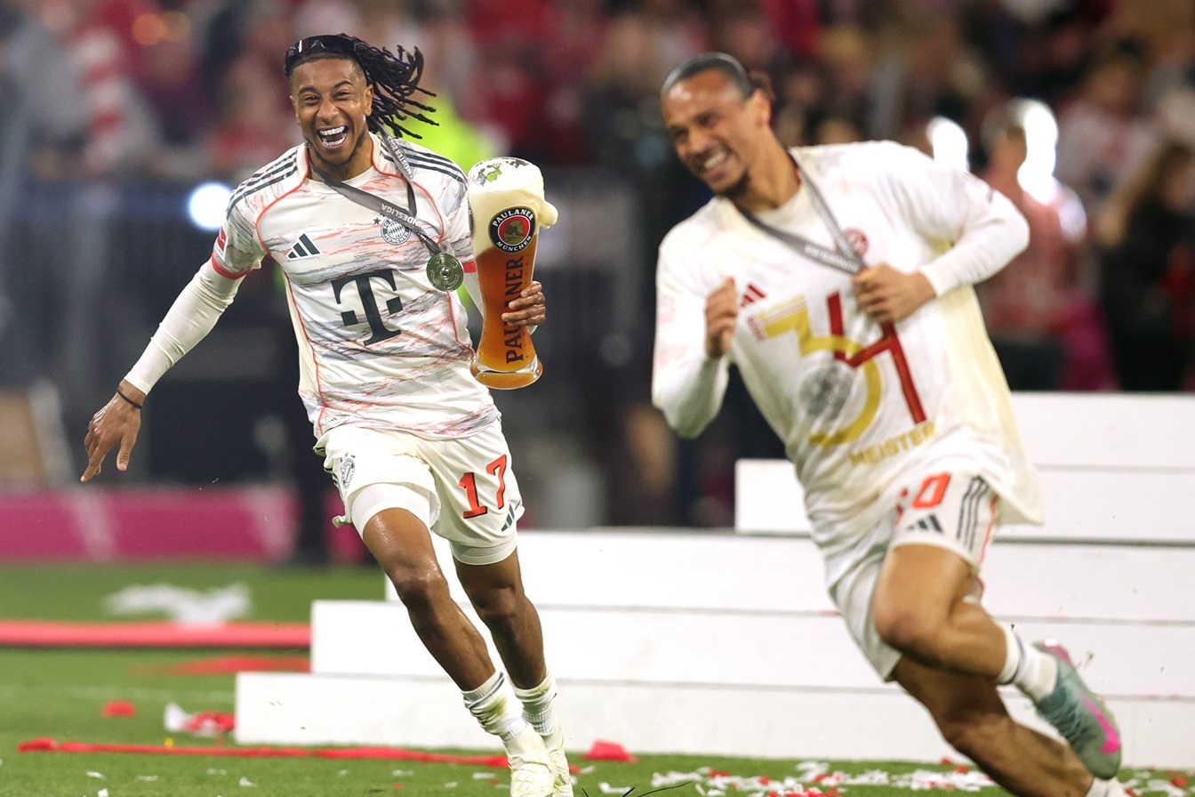 Zwei Fußballspieler feiern mit einem Pokal und Medaillen auf dem Spielfeld.